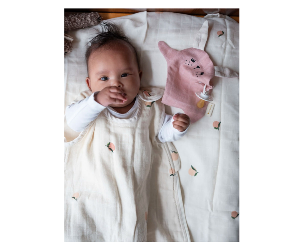 Bebé deitado com vestido creme com flores e véu rosa em forma de animal e chucha