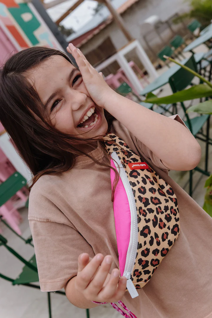 Criança sorridente com pochete padrão leopardo e t-shirt bege num café ao ar livre