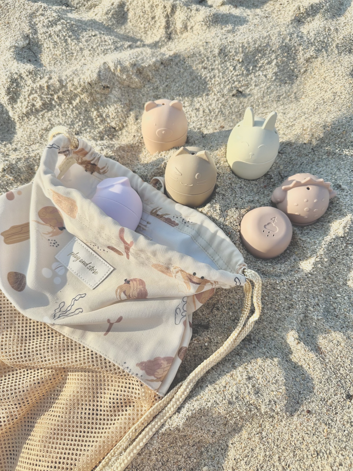Brinquedos de silicone em forma de animais e saco de tecido com padrão na areia