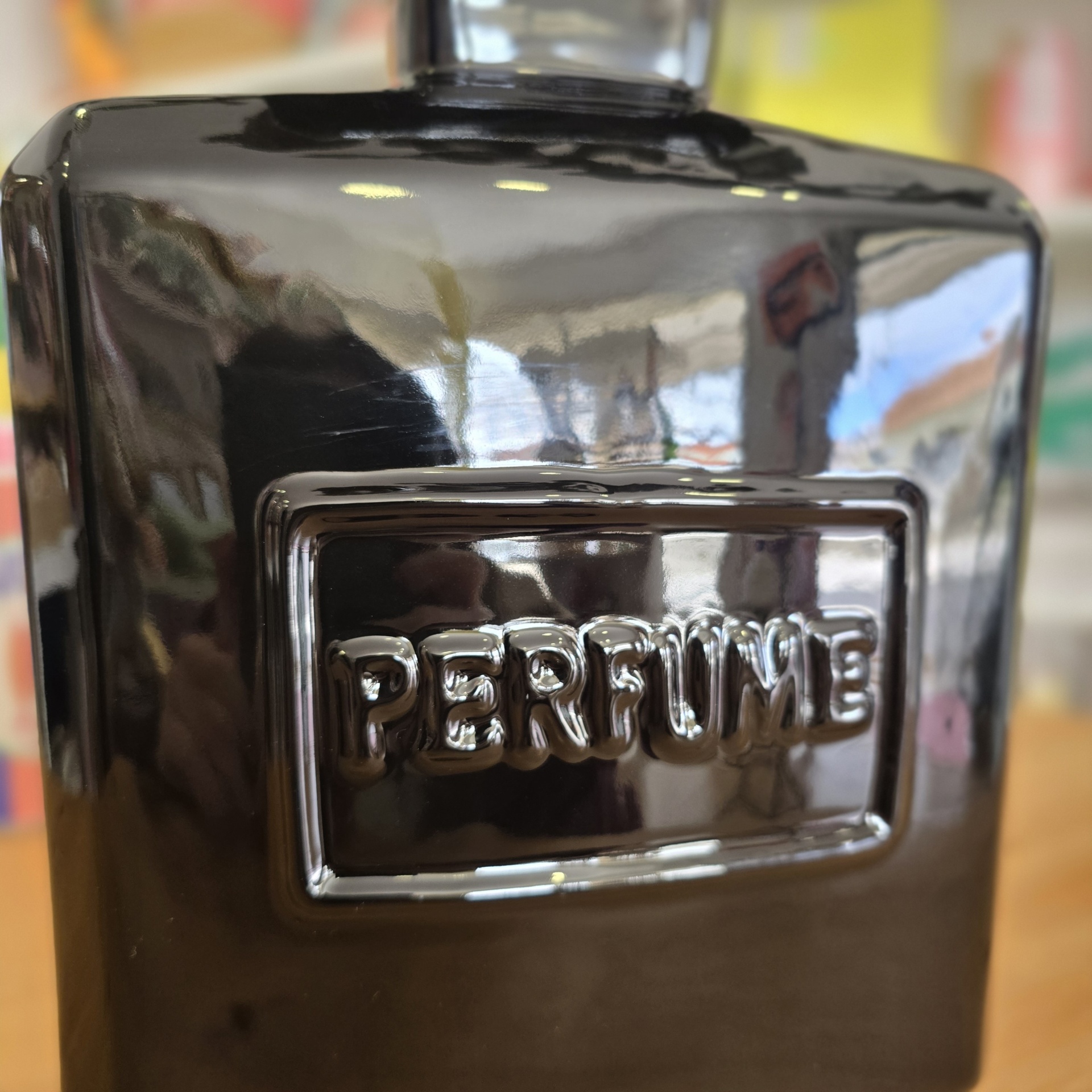Frasco de perfume preto brilhante com palavra PERFUME em relevo
