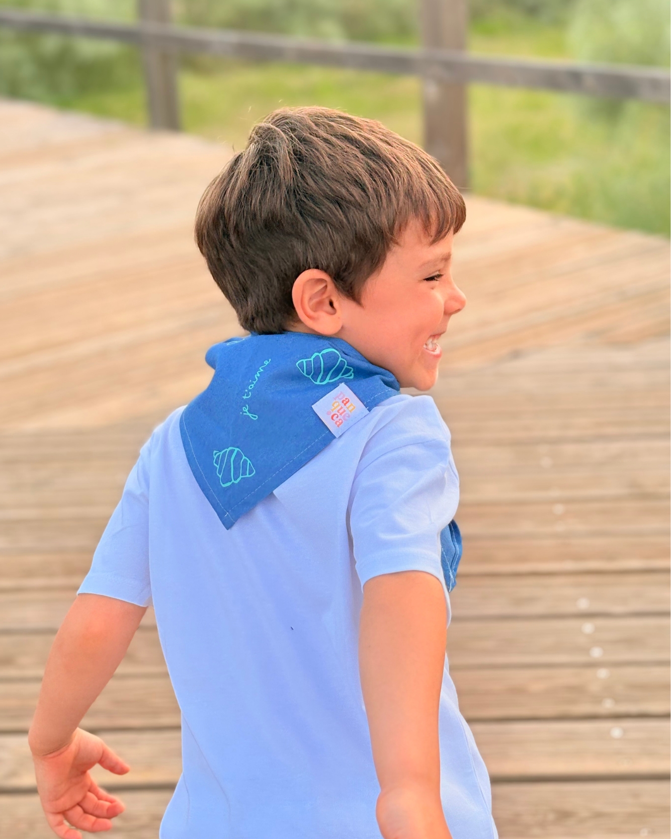 Menino de perfil com lenço azul com croissants e texto em francês