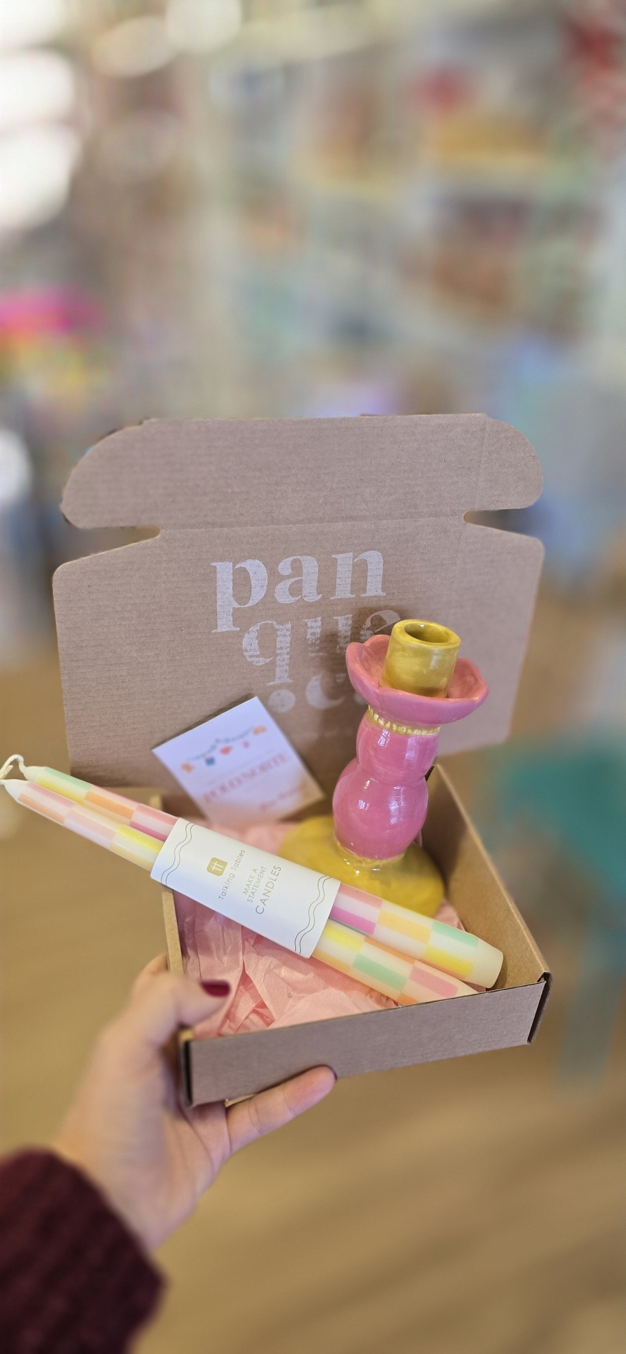 Caixa de cartão aberta com castiçal cerâmico e velas coloridas