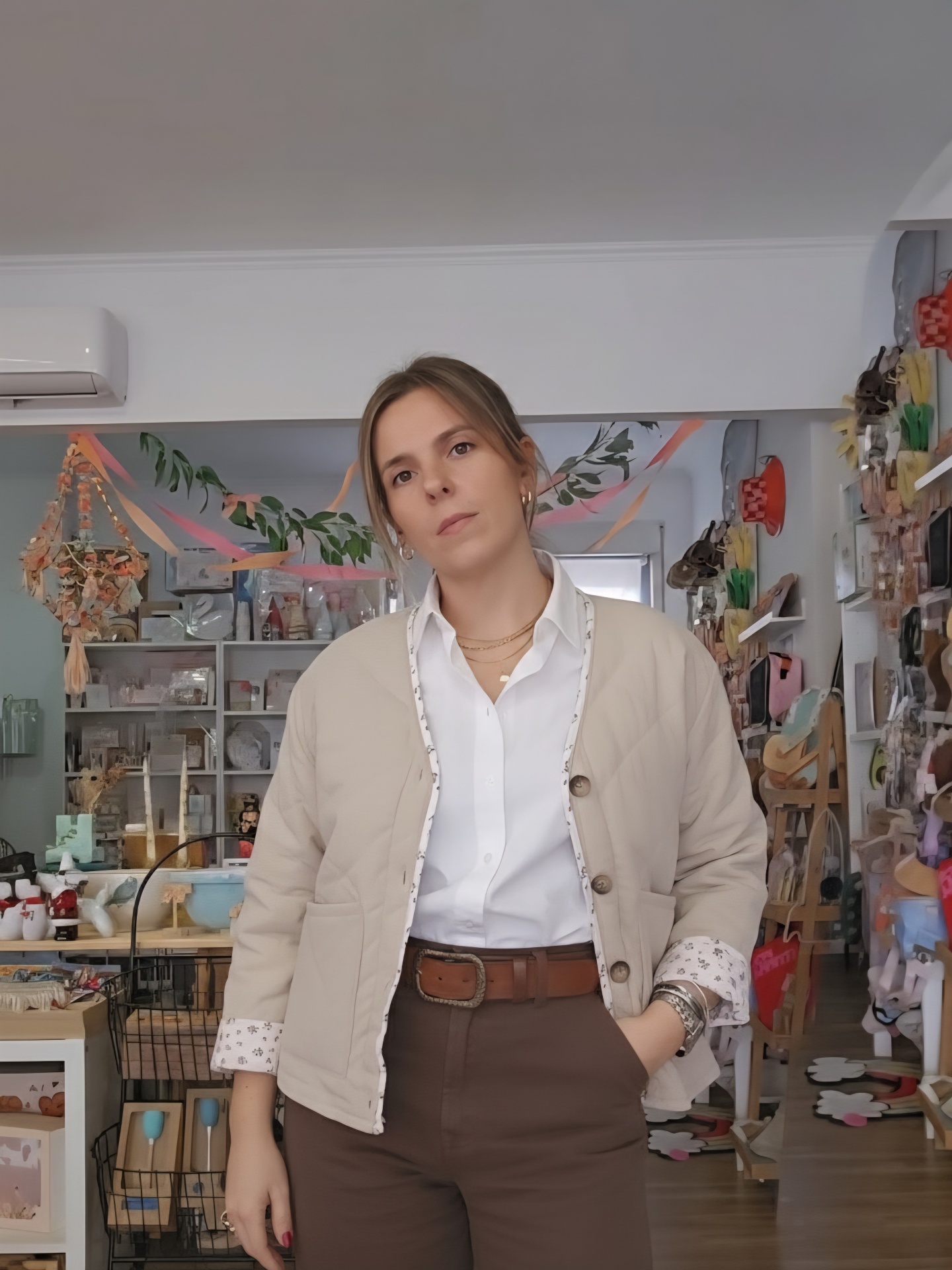 Mulher com casaco bege acolchoado, camisa branca e calças castanhas numa loja decorada