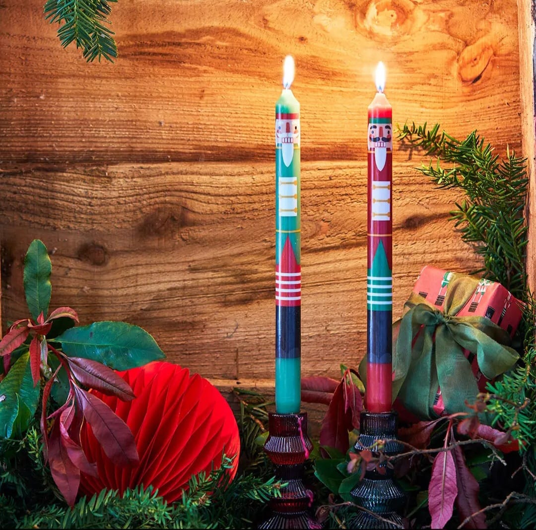Velas decorativas acesas em suportes de vidro com decoração natalícia e elementos naturais sobre fundo de madeira.