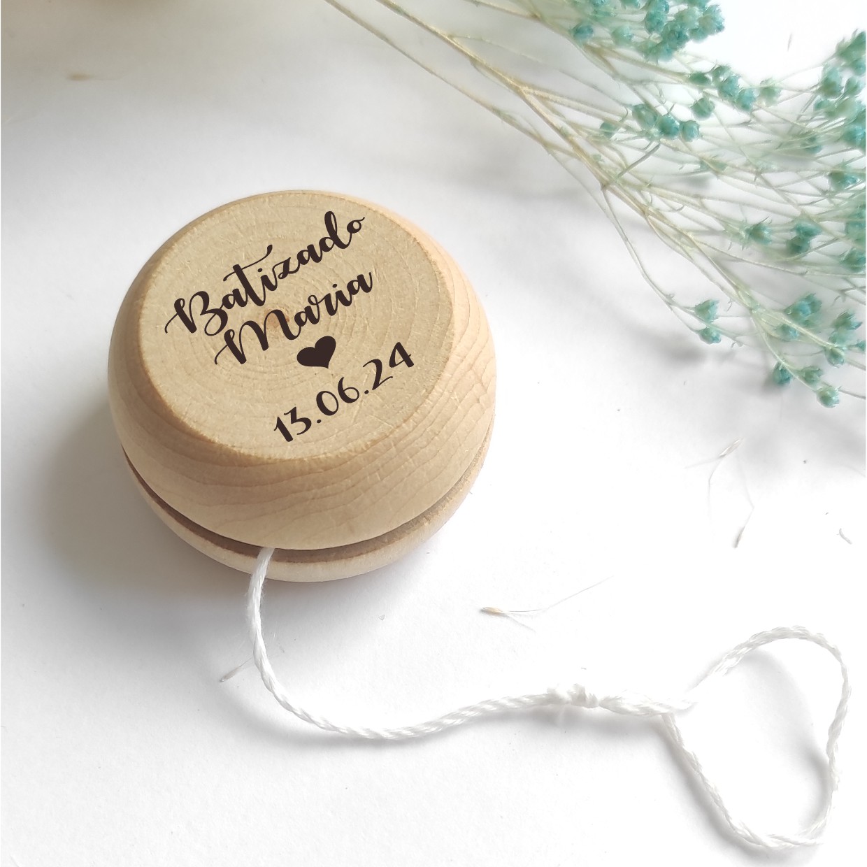 Ioiô de madeira com texto gravado e cordão branco em fundo branco com flores secas
