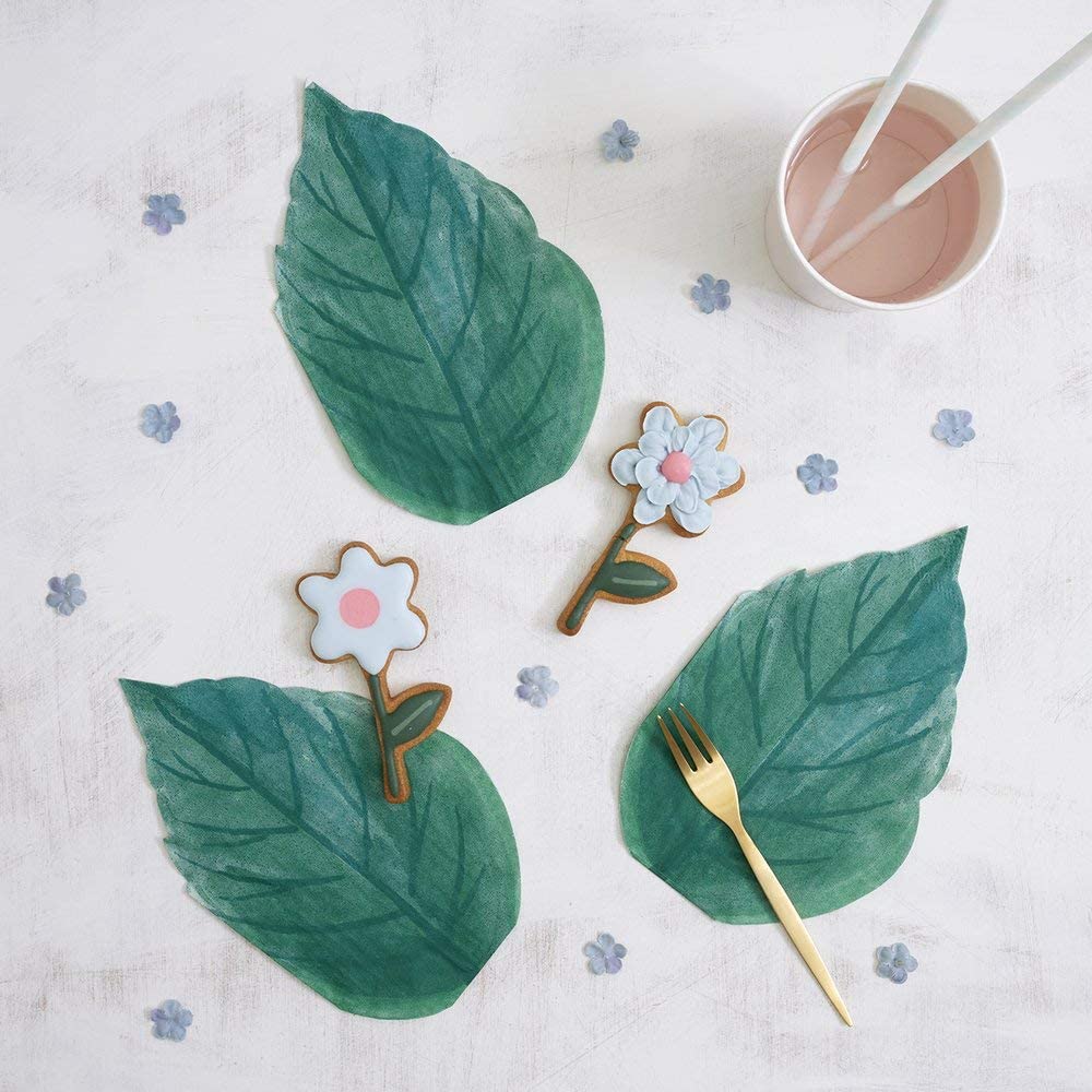 Mesa com folhas verdes, biscoitos florais decorados e copo com bebida cor de rosa