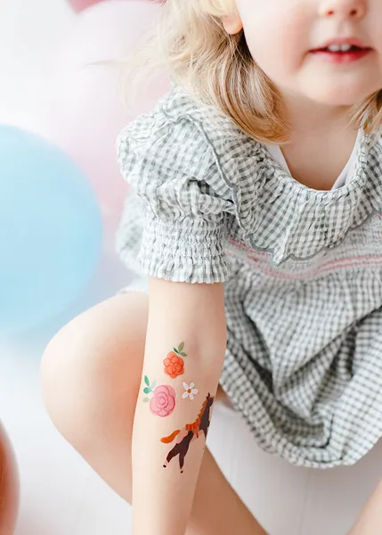 Criança com vestido xadrez cinza e tatuagens temporárias no antebraço