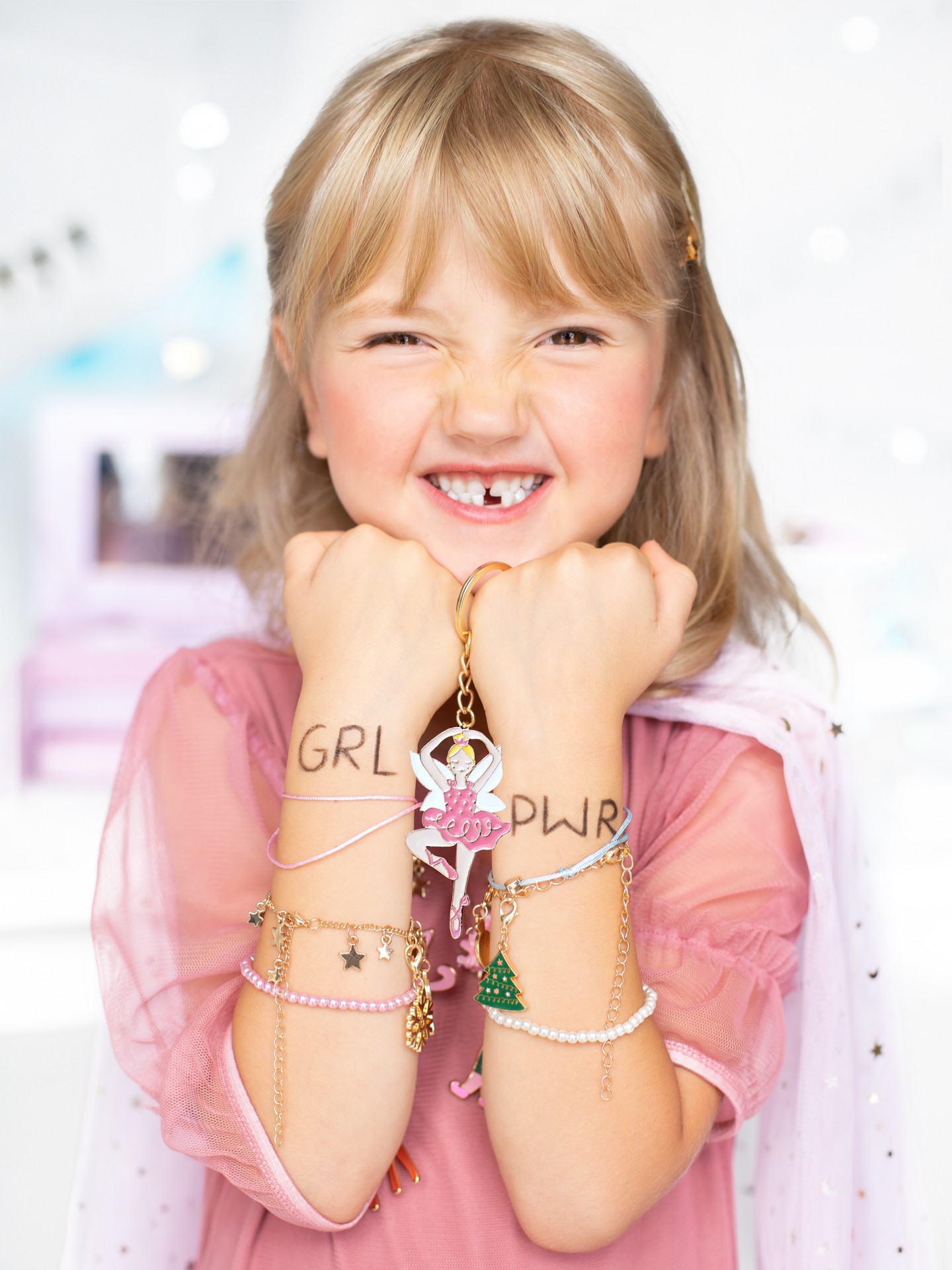 Criança loira com pulseiras e chaveiro de bailarina mostra as mãos com 'GRL PWR' escrito