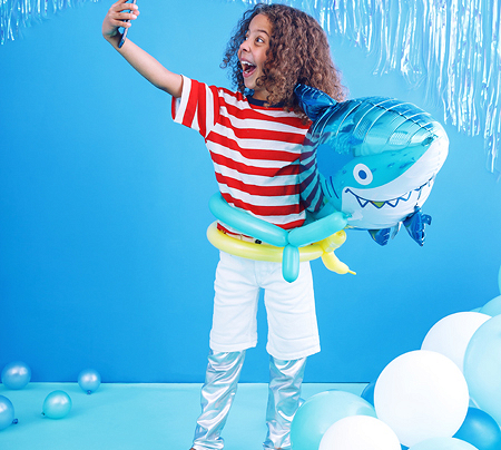 Criança com t-shirt riscada e balões em forma de tubarão no cenário azul