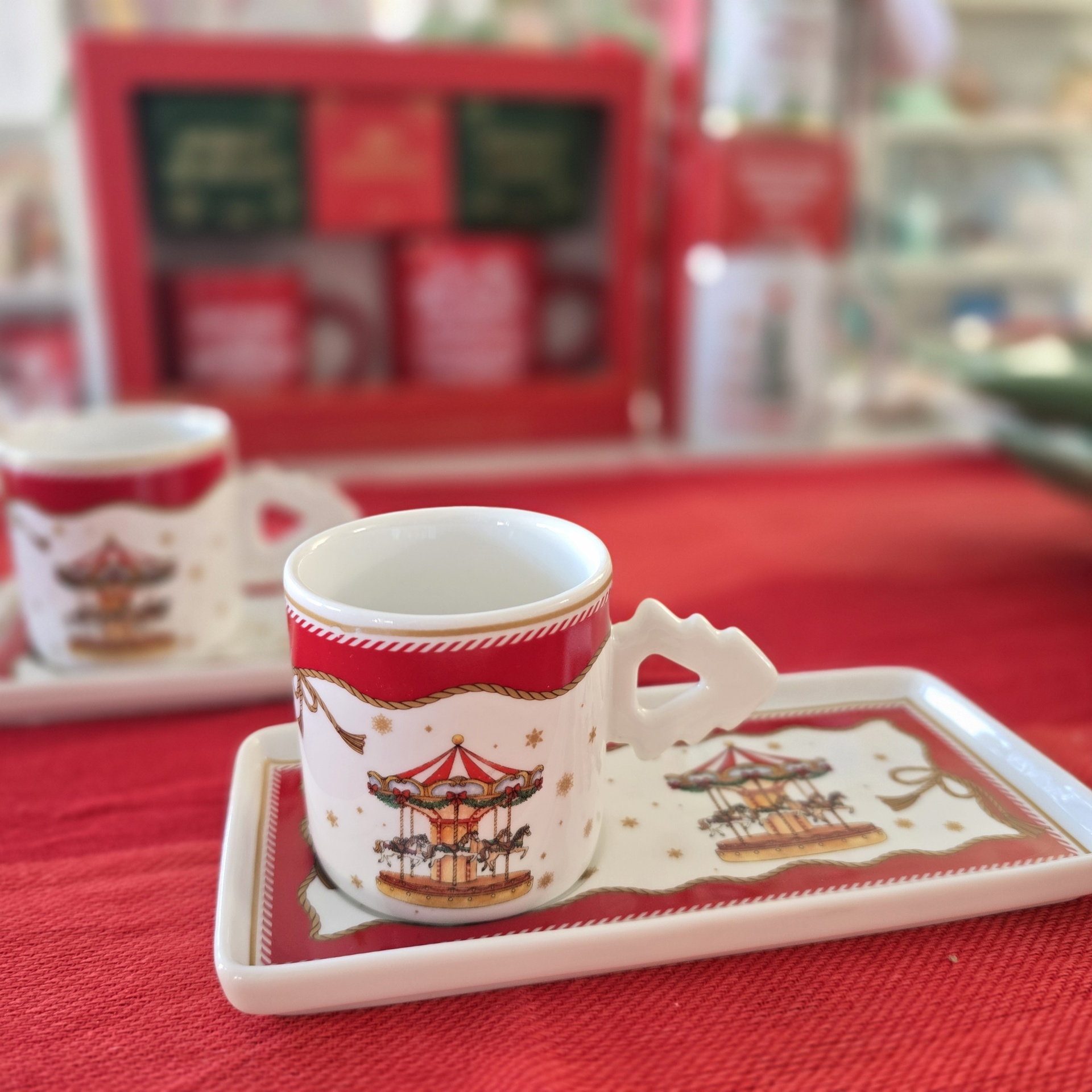 Conjunto de chávenas e prato quadrado decorados com carrossel e motivos natalícios em porcelana branca com detalhes vermelhos e dourados.