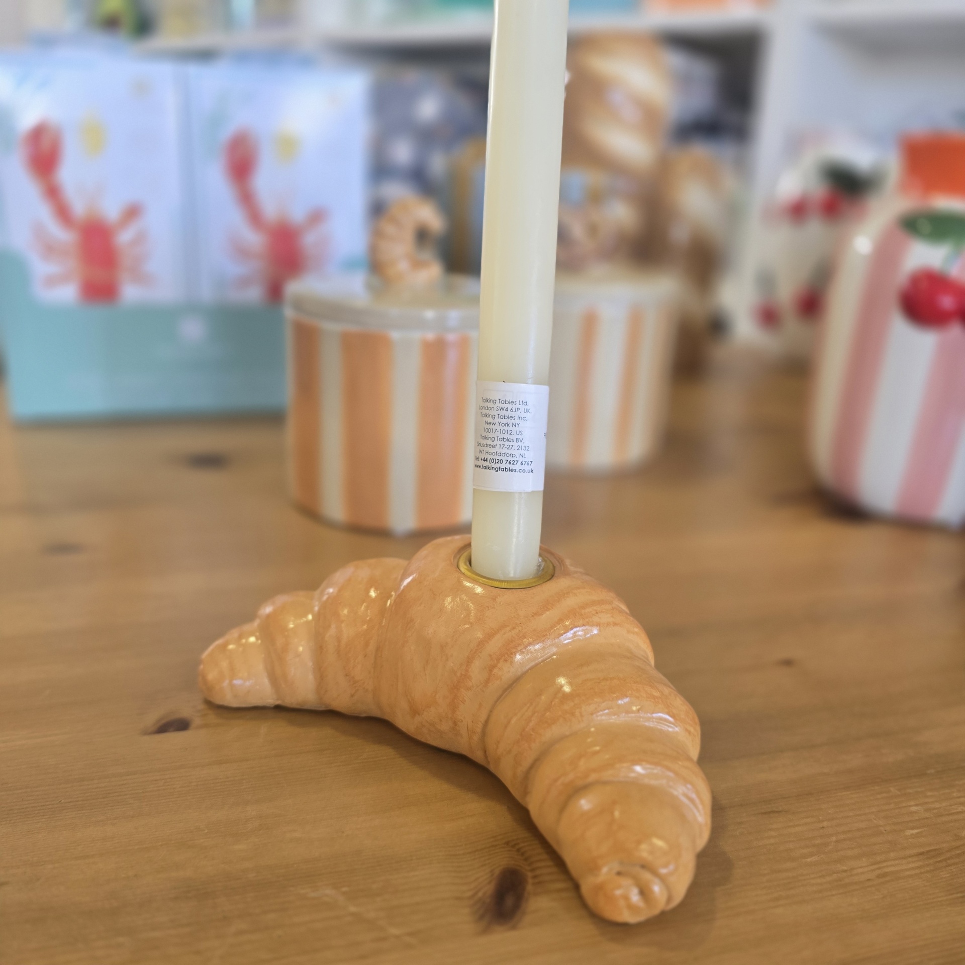 Porta-vela cerâmico em forma de croissant com vela branca numa mesa de madeira.