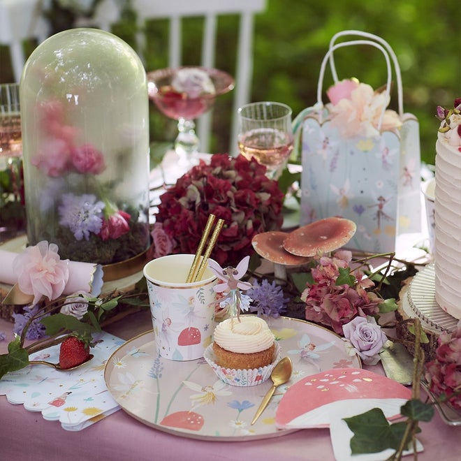 Mesa decorada com cupcake, copo, prato e flores num tema de jardim encantado