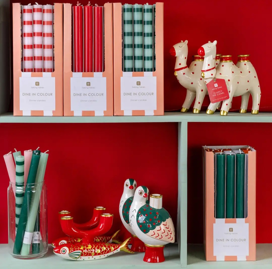 castiçais decorativos e velas coloridas em prateleira com fundo vermelho