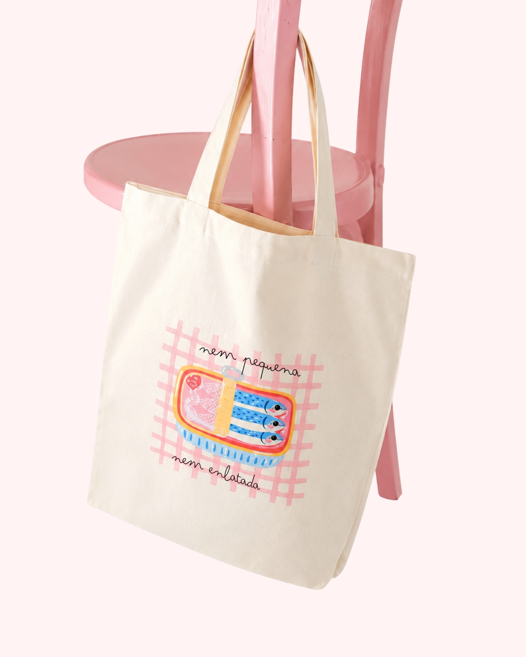 Mala de tecido creme com estampa de lata de sardinhas e texto em letras pretas pendurada numa cadeira rosa
