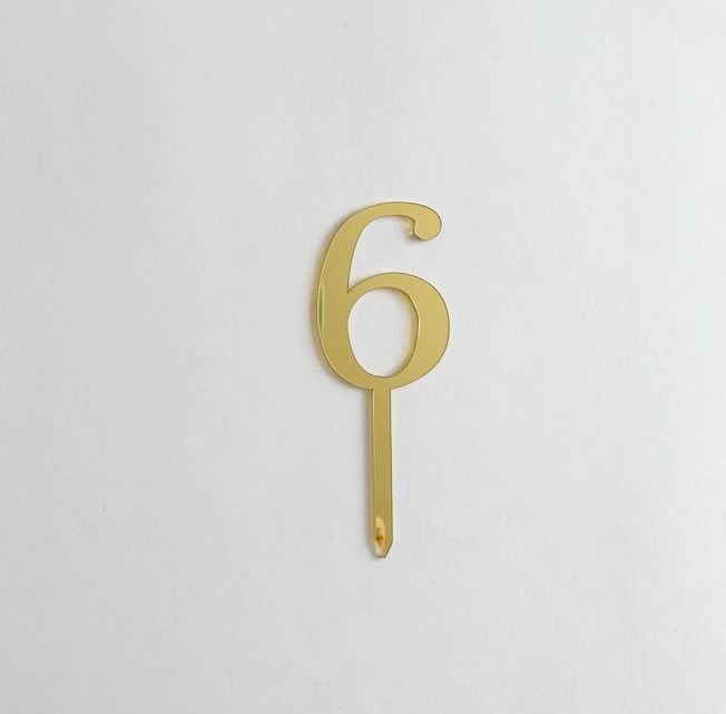 Número 6 dourado metálico com base estreita sobre fundo branco