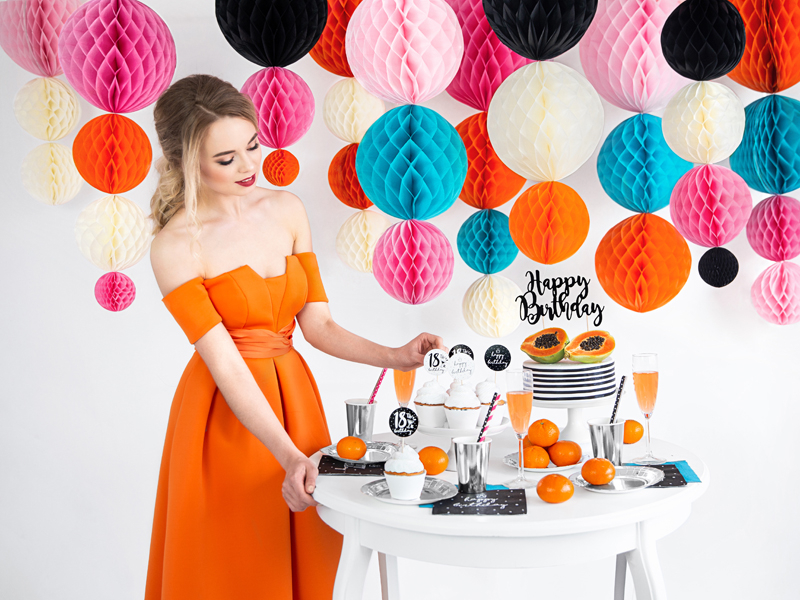 Mulher de vestido laranja com decoração colorida de aniversário e mesa com bolo e tangerinas