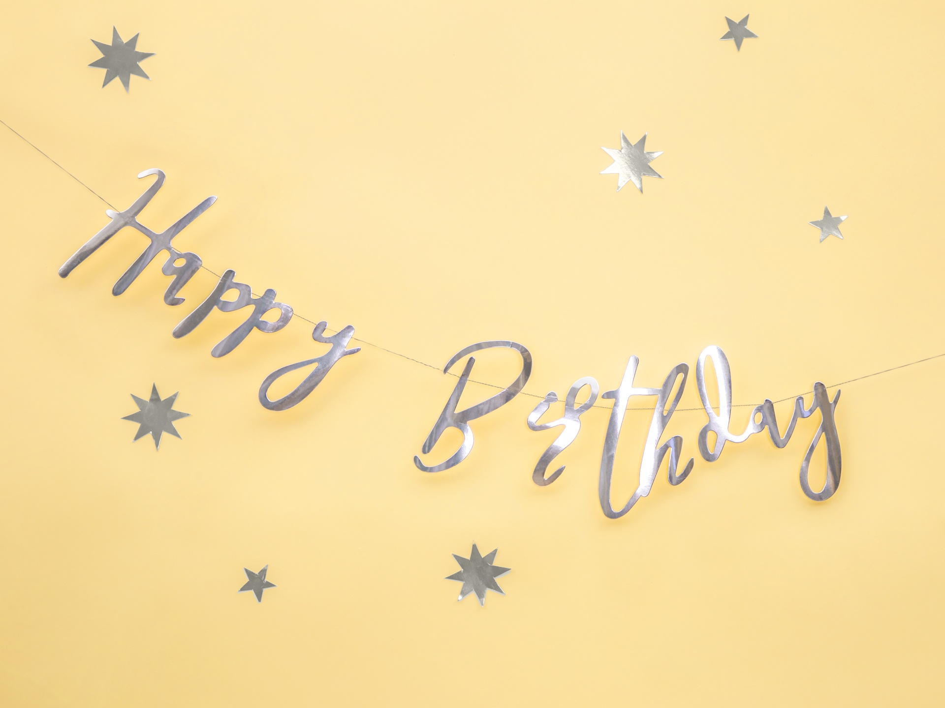 Decoração prateada com texto Happy Birthday sobre fundo amarelo com estrelas prateadas