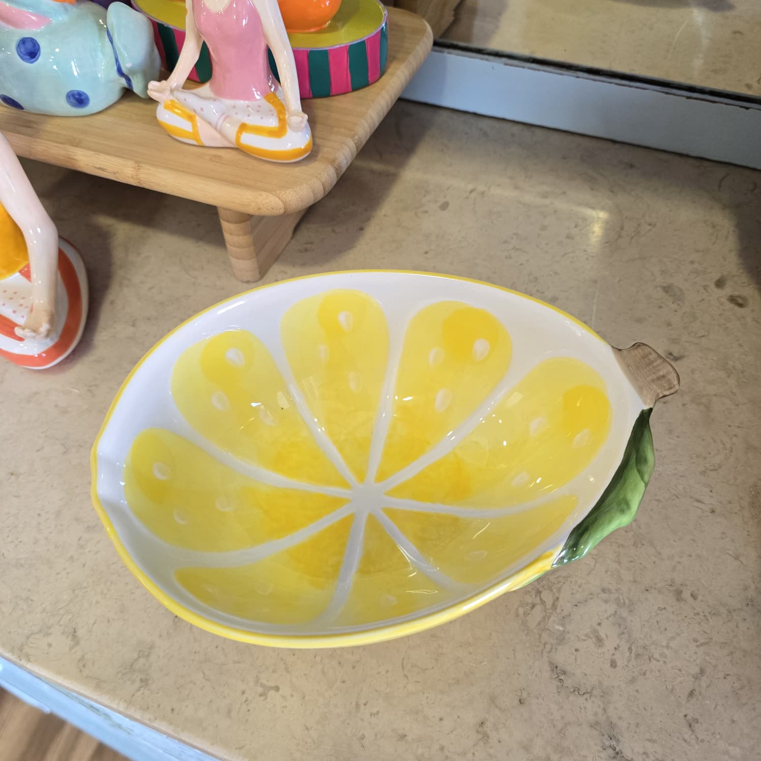 Taça em cerâmica amarela em formato de fatia de limão com relevo verde na borda.