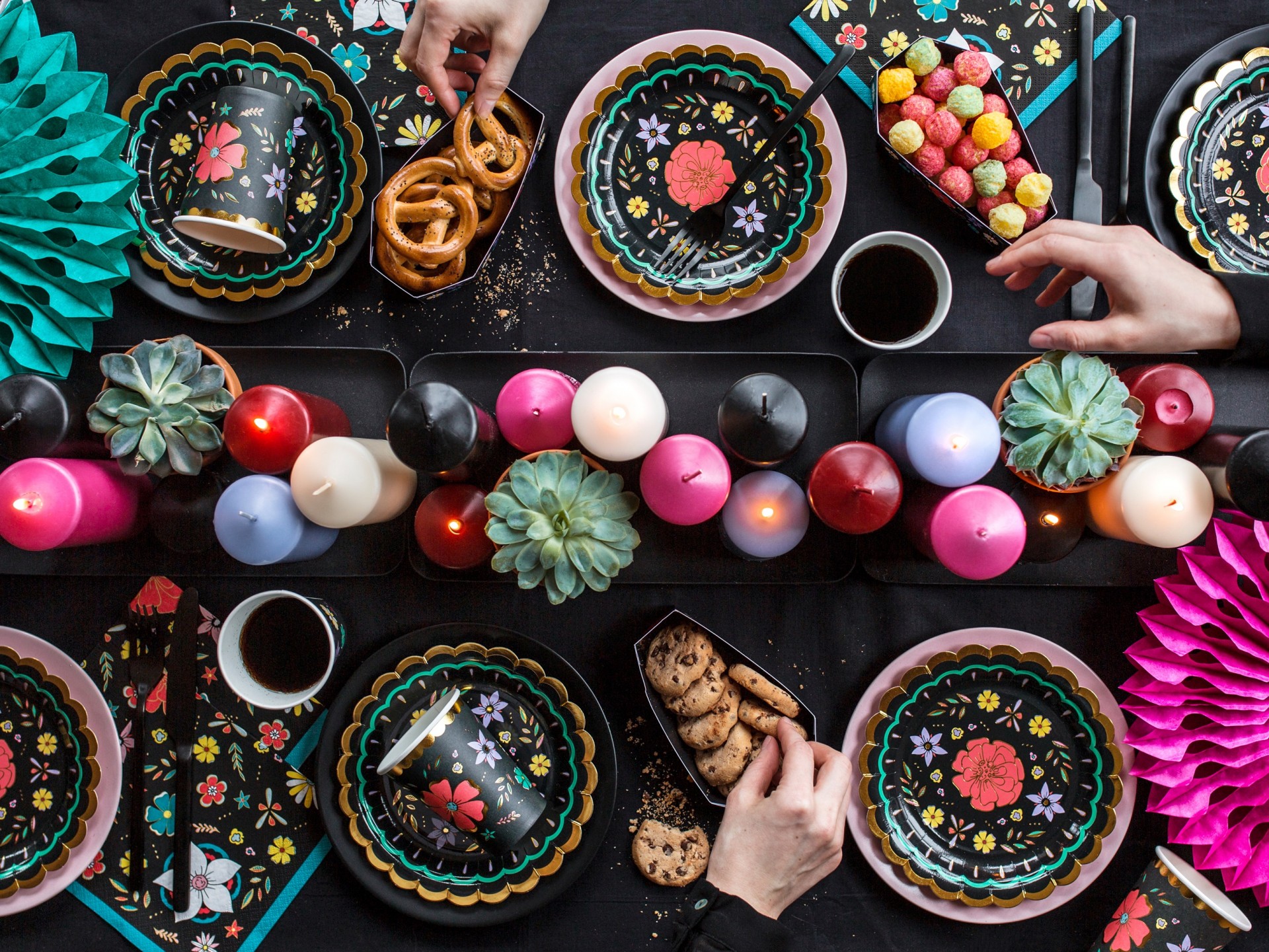 Mesa decorada com pratos, copos, velas e flores coloridas para festa