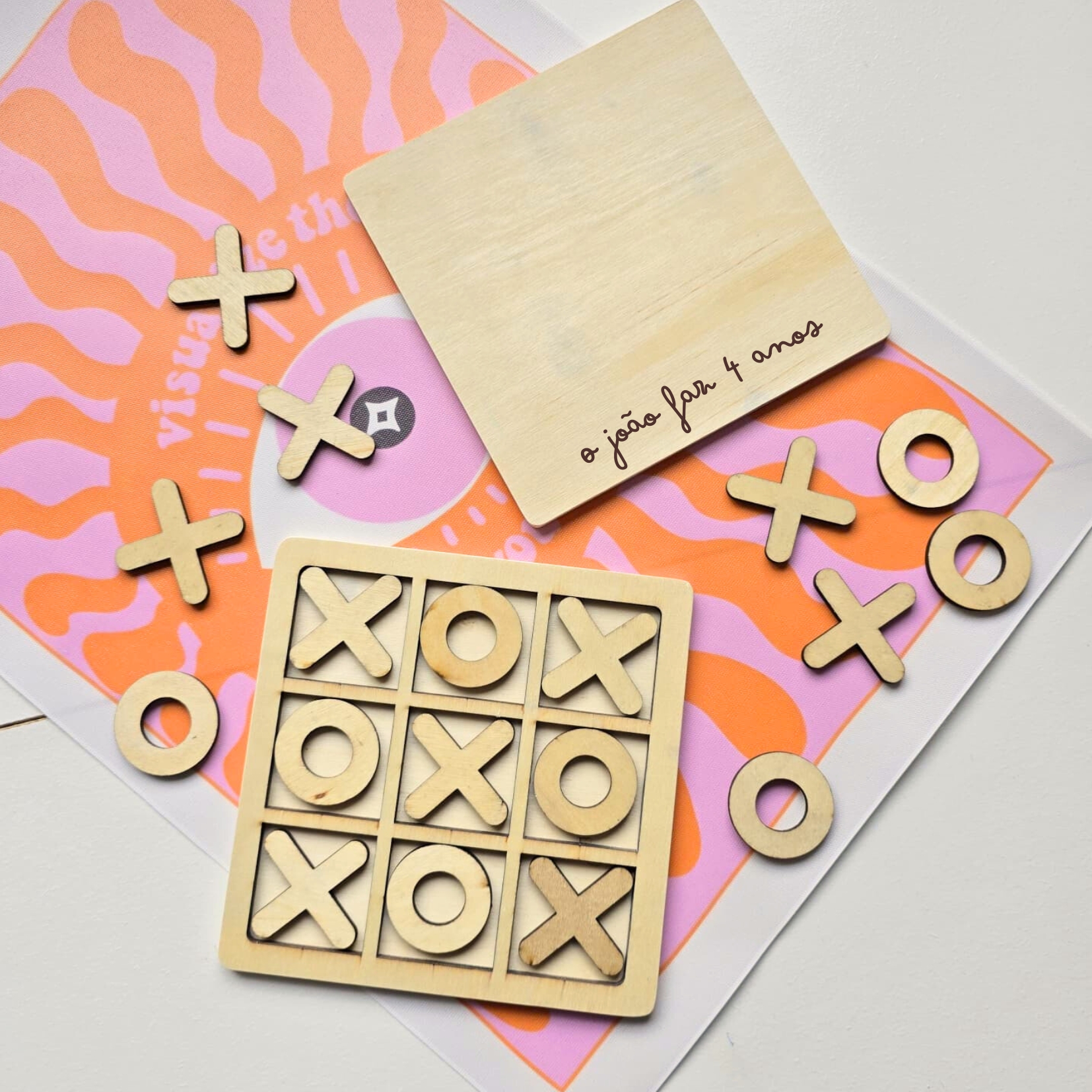 Jogo da velha em madeira com peças X e O sobre pano colorido