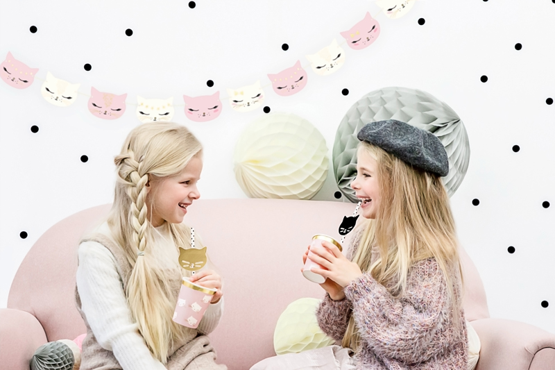 Duas raparigas sentadas num sofá cor-de-rosa a beber de copos decorados com gatos