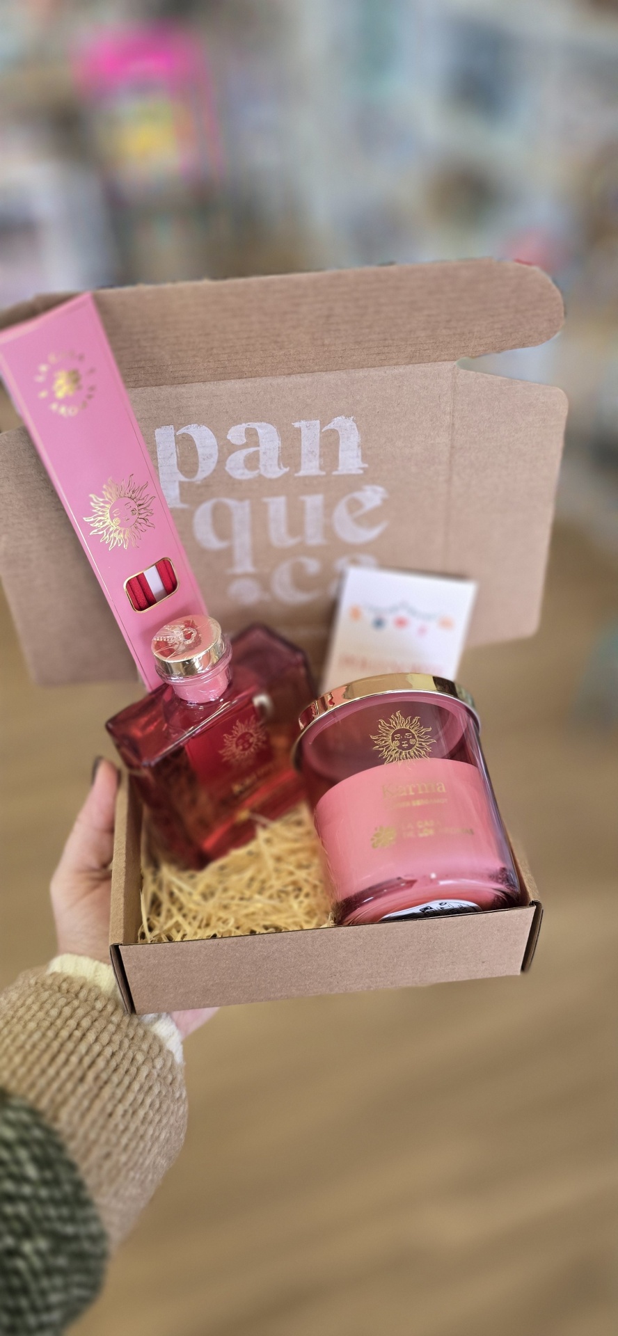 Conjunto de produtos rosa com detalhes dourados embalados numa caixa de cartão castanho.