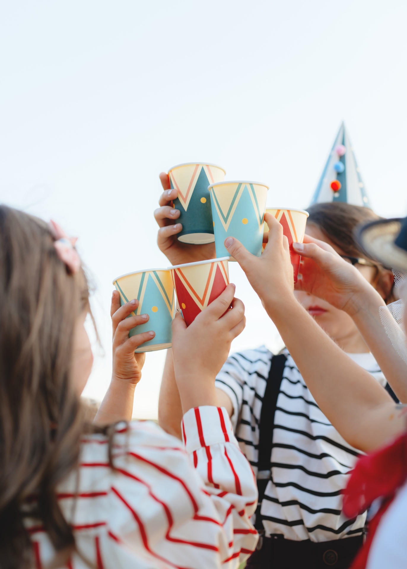 Crianças a brindar com copos de papel de padrões geométricos em festa ao ar livre