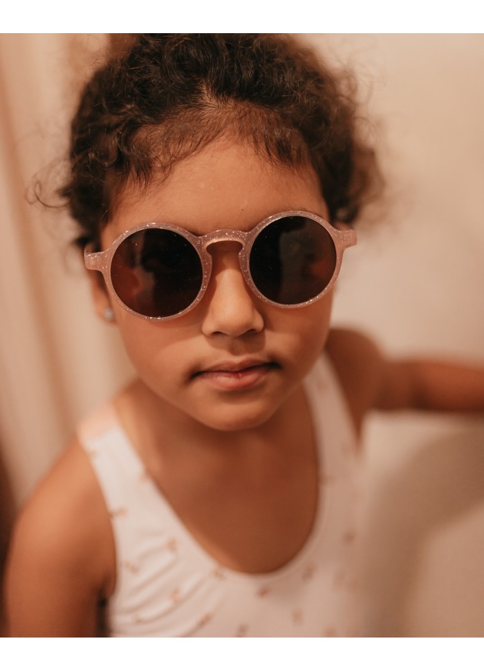 Criança a usar óculos de sol redondos cor de rosa com brilho