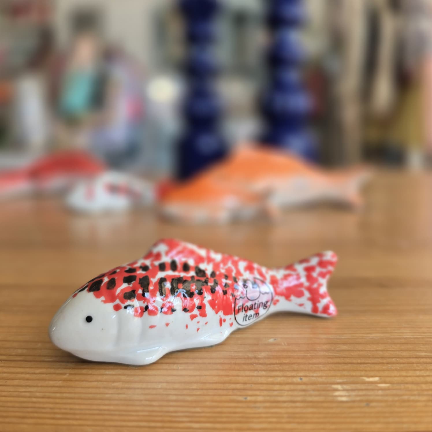 Peixe cerâmico decorativo branco com manchas vermelhas e pretas sobre superfície de madeira