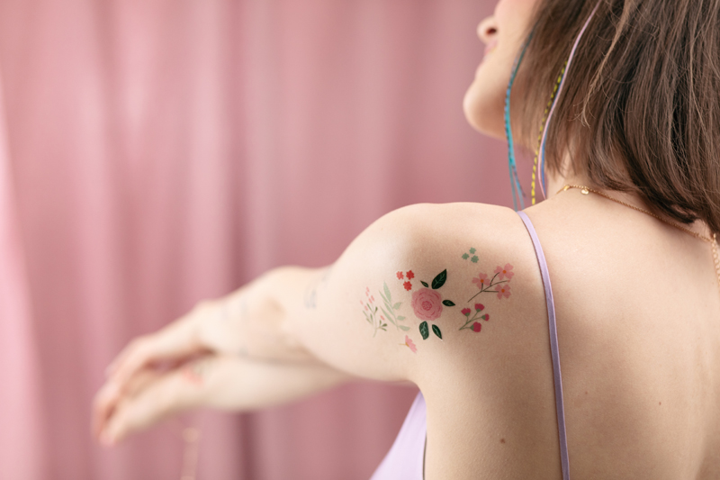 Tatuagem de flores coloridas no ombro esquerdo de mulher com top lilás