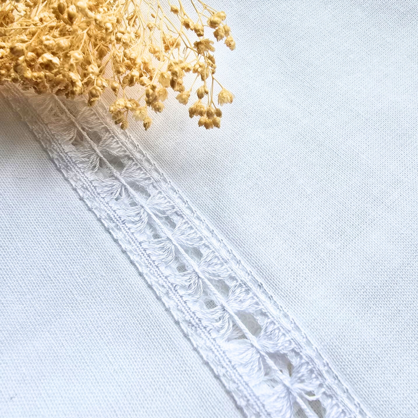 tecido branco com renda branca e flores secas cor bege no canto superior esquerdo