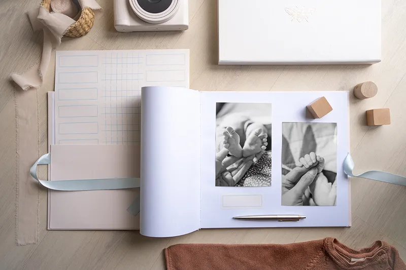 Livro com fotos de pés de bebé em superfície clara com objetos ao redor