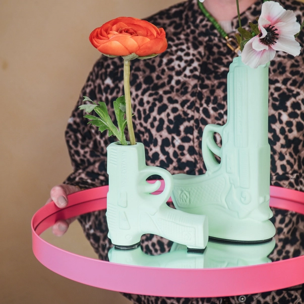 Duas jarras verdes em forma de pistola com flores, em tabuleiro rosa com espelho