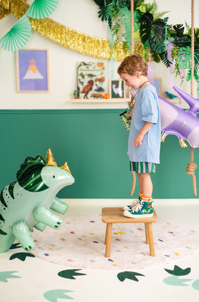 Criança em sala decorada com balões de dinossauro e unicórnio e decoração festiva