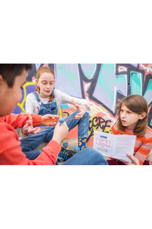 Crianças brincando com fios coloridos e folheto em parede com grafiti