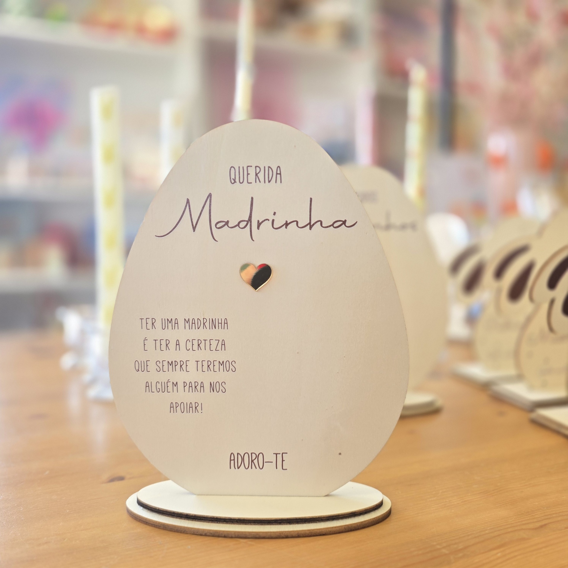 Prenda decorativa em madeira com texto para madrinha sobre mesa de madeira.