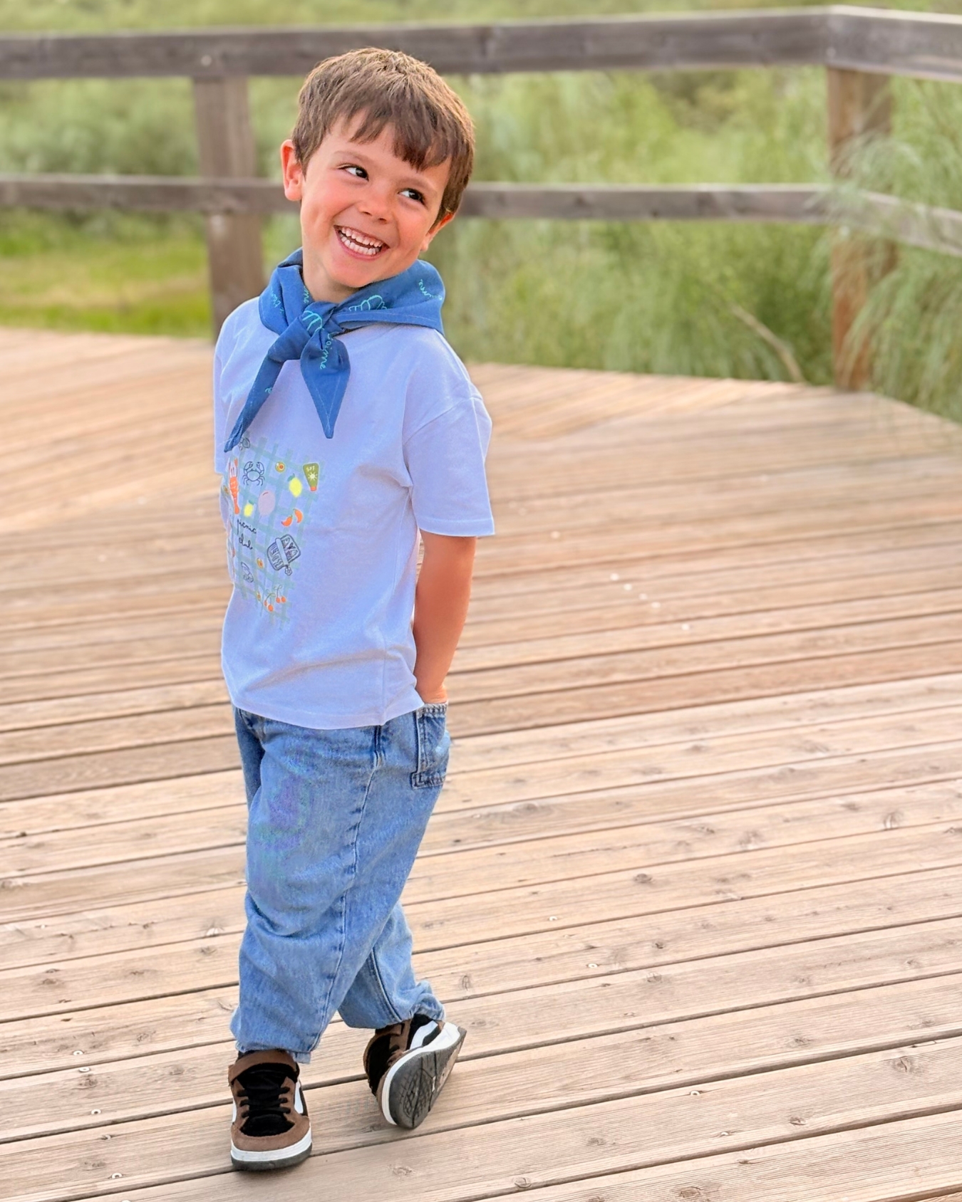 Criança sorridente com roupa casual colorida ao ar livre sobre madeira
