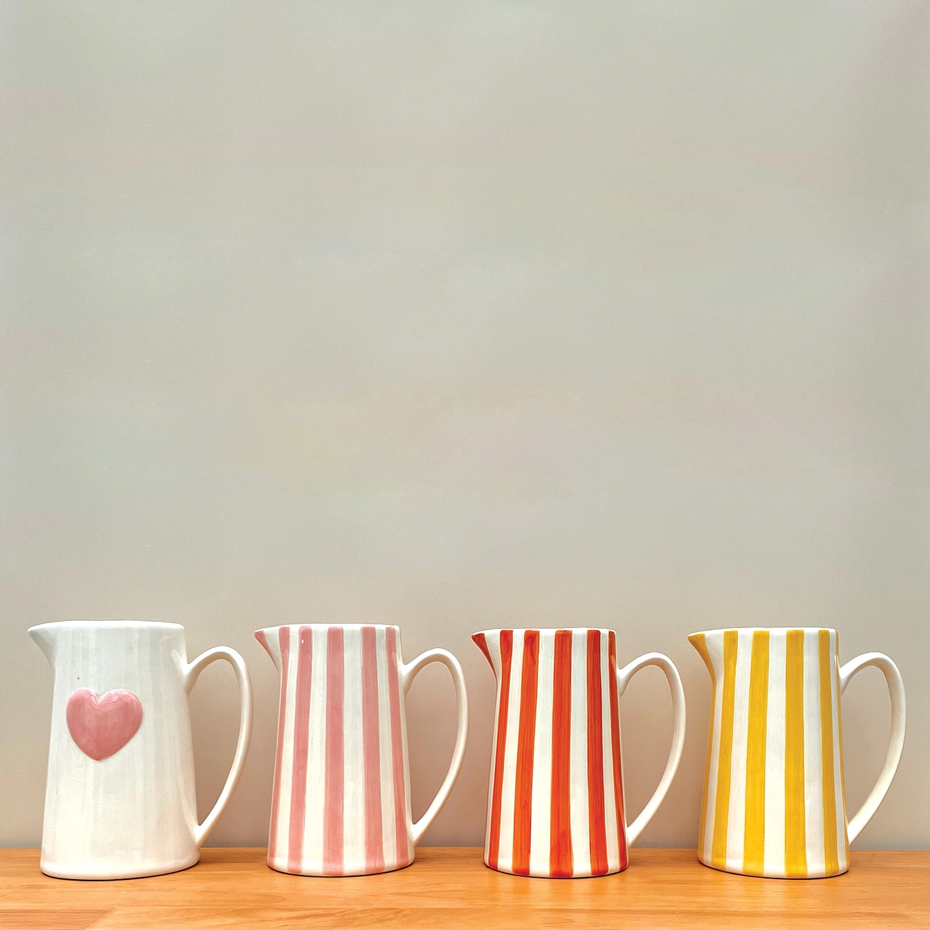 Quatro jarros de cerâmica com riscas coloridas e um com coração cor de rosa.