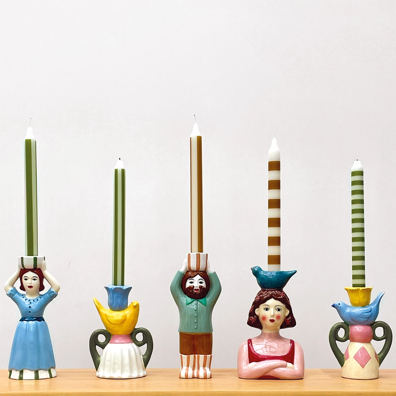 Castiçais de cerâmica coloridos com velas às riscas em diferentes designs de figuras humanas e pássaros.
