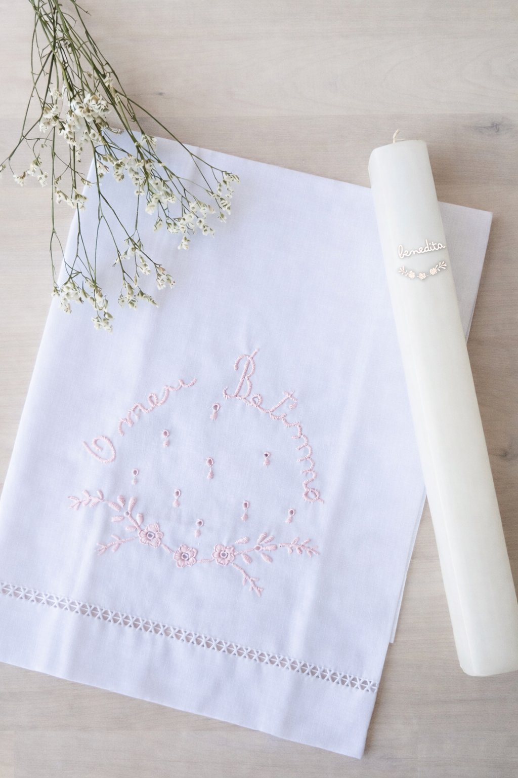 Toalha branca bordada com frase O meu Batismo e vela branca com etiqueta benedita em superfície de madeira