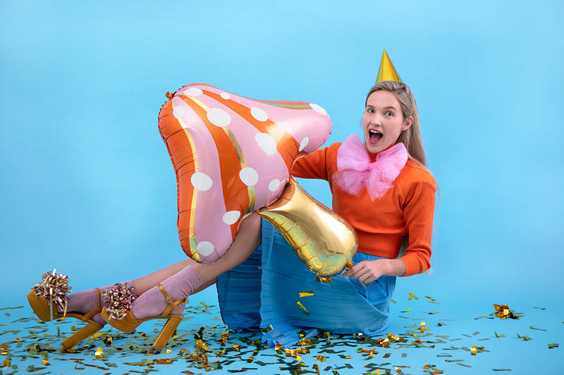 Mulher em roupa colorida com balões metalizados e confetes, em fundo azul