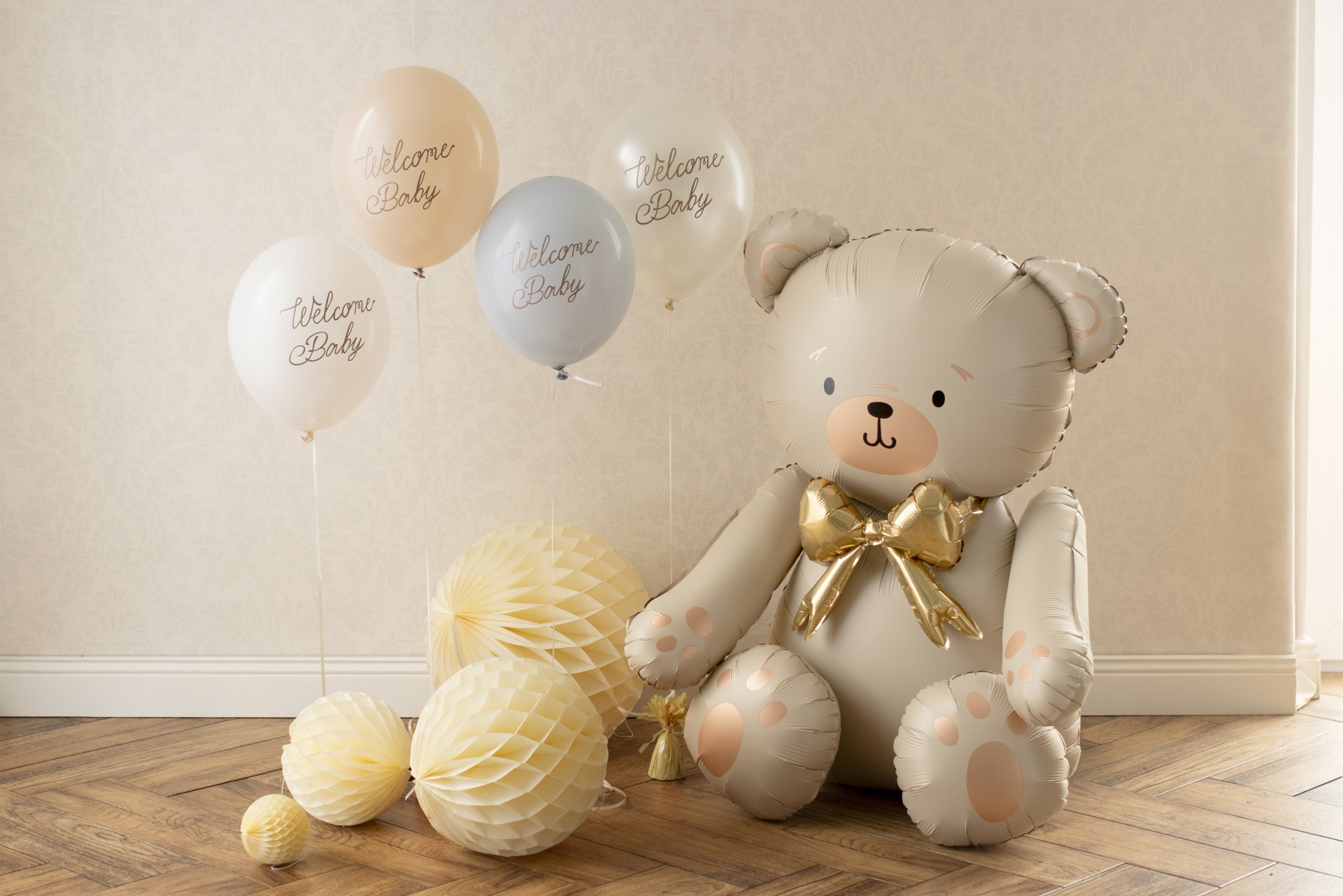 Decoração para bebé com balões e balão em forma de urso sobre chão de madeira e parede clara
