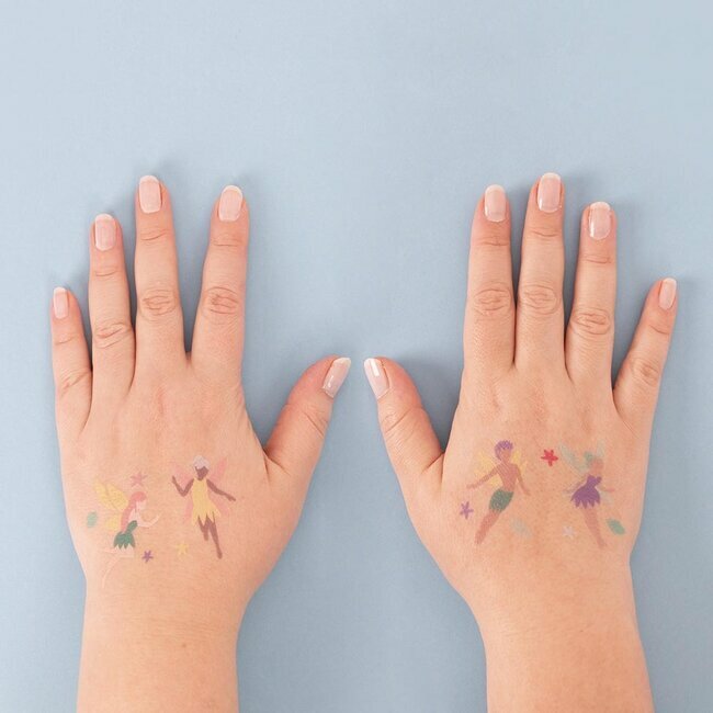 Mãos femininas com tatuagens temporárias de fadas sobre fundo azul
