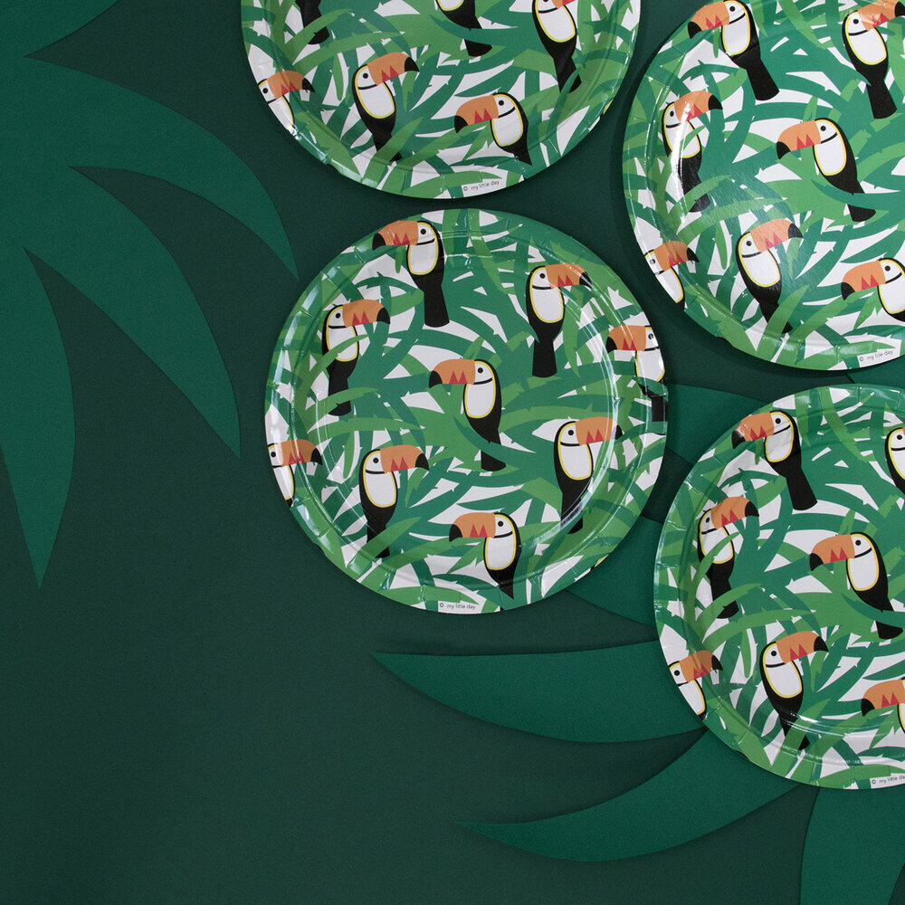 Pratos de papel com padrão de tucanos e folhas verdes sobre fundo verde escuro