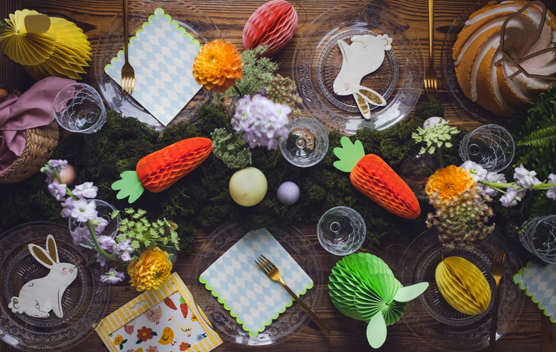 Mesa decorada para festa com guardanapos, cupcakes, flores e enfeites de papel em forma de coelho e cenoura