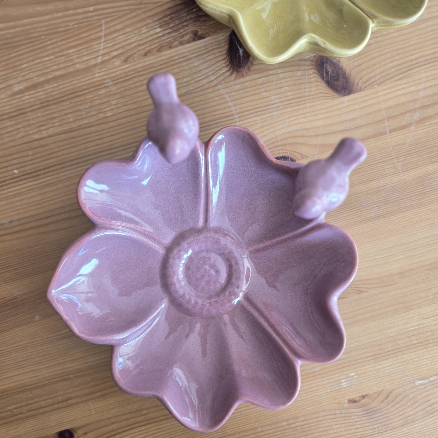 Pratos de cerâmica em forma de flor com pássaros no rebordo sobre mesa de madeira