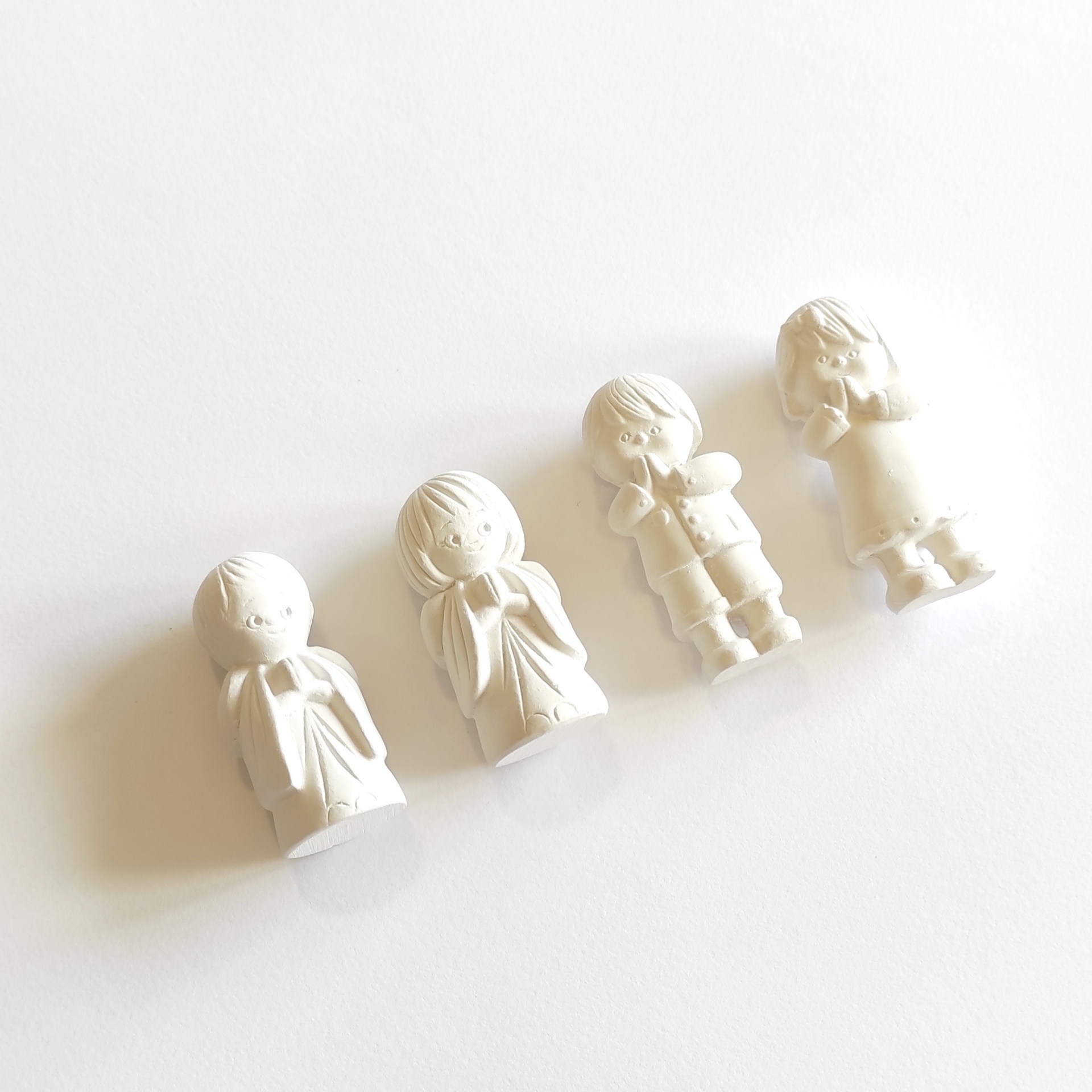 Quatro estatuetas decorativas brancas representando figuras humanas em oração.