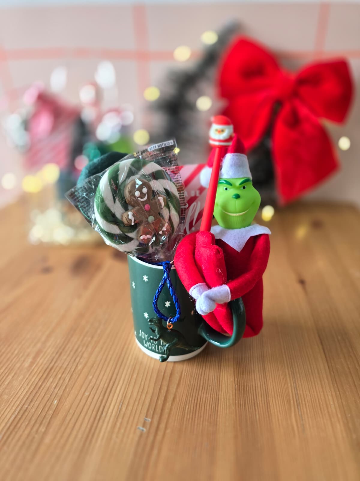 Caneca verde com pirulito, caneta com topo de Natal e boneco do Grinch em feltro numa mesa de madeira