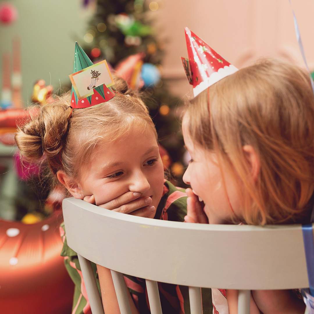 Duas crianças com chapéus de festa em ambiente de Natal