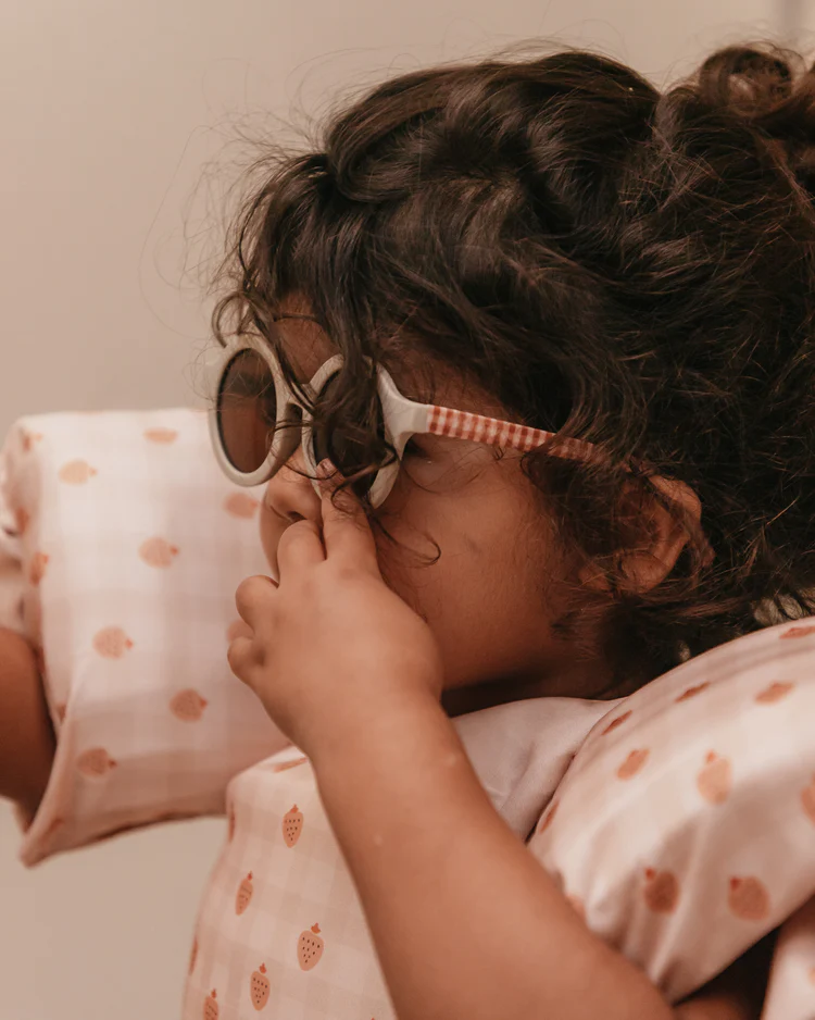 Criança com colete de natação rosa com estampado de morangos e óculos de sol redondos.